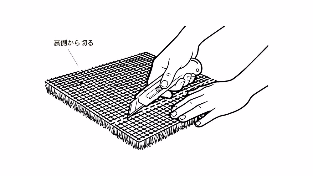 人工芝を裏返し、裏側からカッターの刃を入れて切っている図