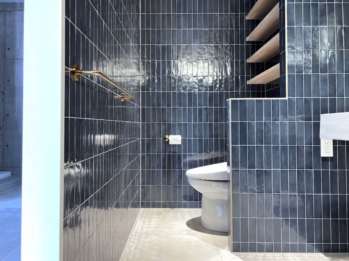ブルータイルの壁が続くトイレスペースと、ゴールドのペーパーホルダー