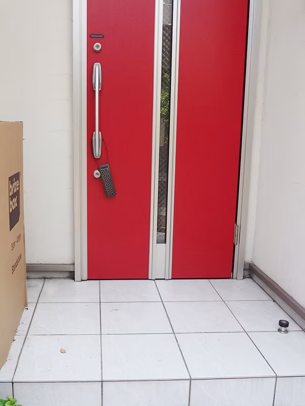 赤い玄関ドアの前に届いた、宅配ボックス本体の梱包
