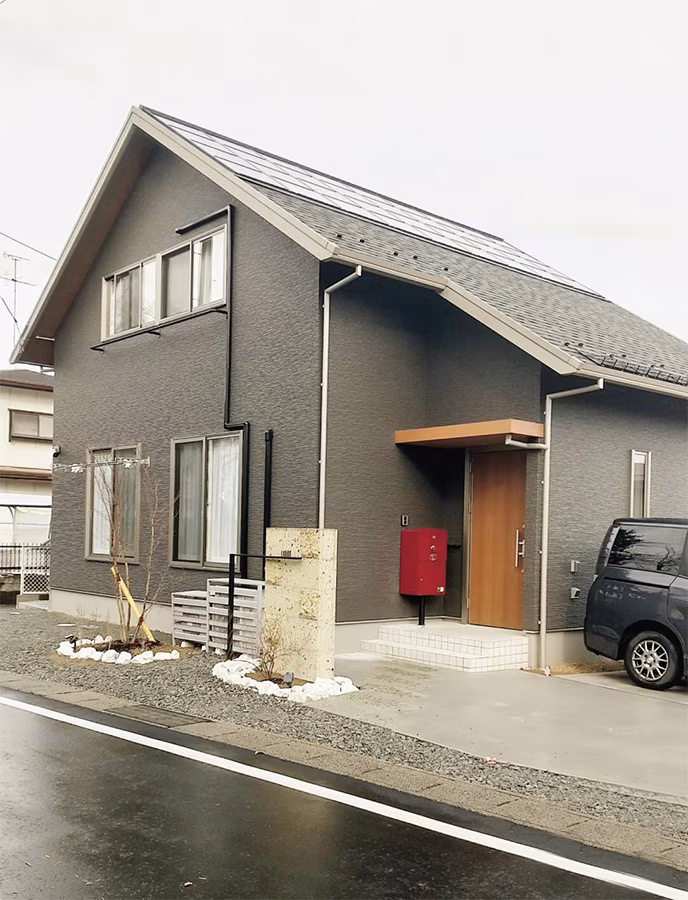 グレーの外壁の住宅の玄関前に、ポール施工したボルドーの宅配ボックス