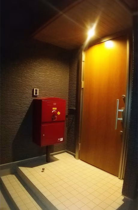 灯りのともる玄関の脇に立つ、ボルドーの宅配ボックス
