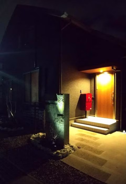 夜の玄関まわり。外灯に照らされたボルドーの宅配ボックスと植栽